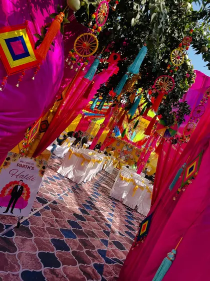 An immersive entrance for a traditional Haldi. The walkway is decorated with bright pink and yellow drapes, tassels, and other folk elements, making guests feel like they've stepped into a vibrant celebration.