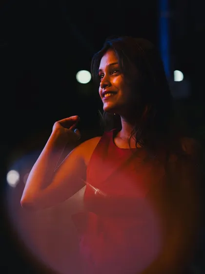 A candid and joyful night portrait of a woman smiling, with colorful light flares in the foreground. This image captures a moment of happiness with a creative and artistic touch.