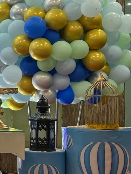 A hot air balloon themed party detail, with decorative props and a balloon arrangement in blue, white, and gold.
