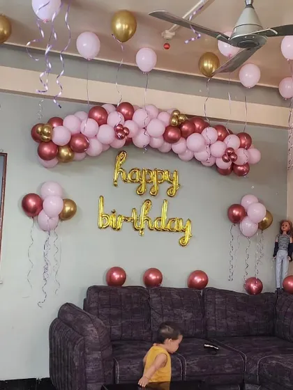 A living room decorated for a birthday with a rose gold and pink balloon arch over the sofa and 'Happy Birthday' foil letters.