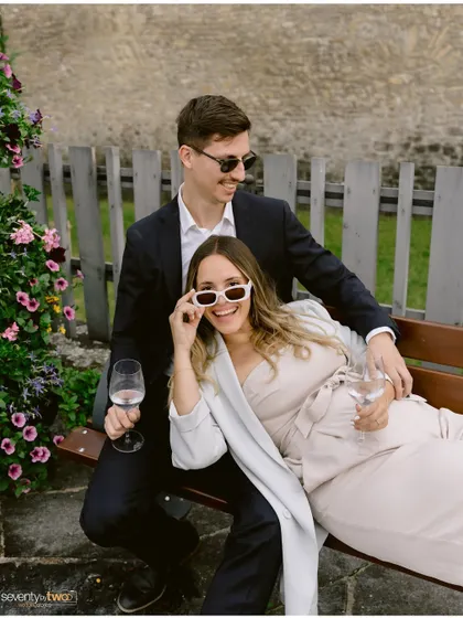 Relaxing on a bench with wine, sunglasses, and big smiles. This portrait is effortlessly cool and full of personality, capturing a moment of fun during their Swiss engagement shoot.