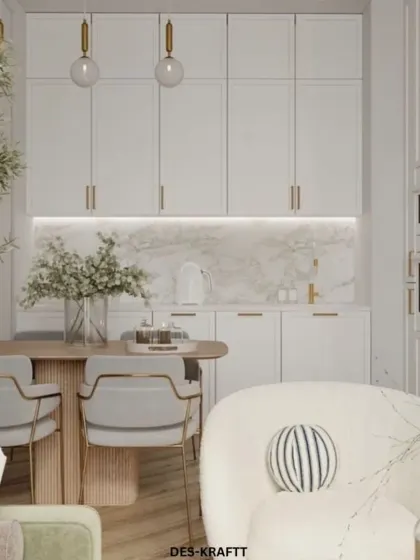 A bright, all-white kitchen is warmed by gold hardware and a natural olive tree. The design seamlessly integrates with the living area for a cohesive, open feel.