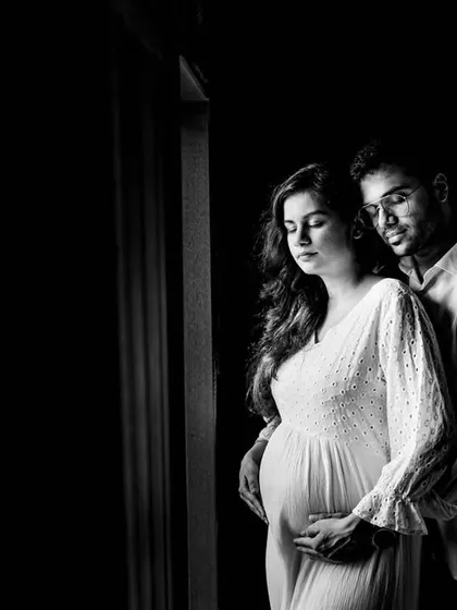 An intimate black and white maternity portrait of a couple. The soft window light and close embrace create a feeling of warmth and anticipation as they await their new arrival.