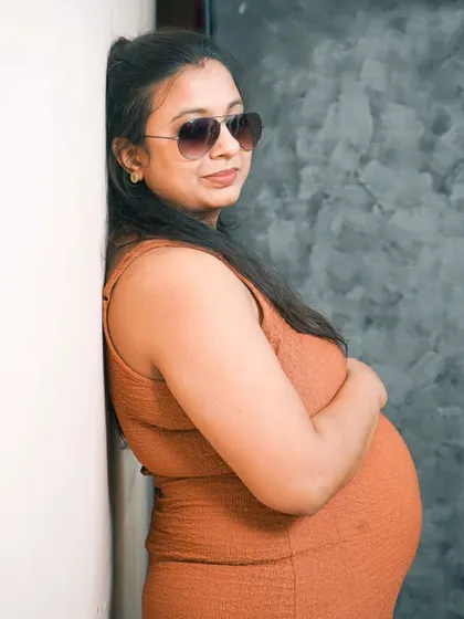 A stylish and modern solo maternity portrait. The simple pose against a textured studio background highlights the beautiful silhouette of the mother-to-be.