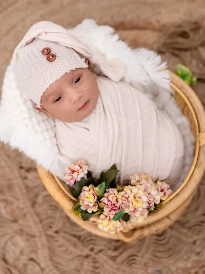 Snuggled in a woven basket with delicate flowers. This newborn portrait combines soft textures, from the knit hat to the fluffy blanket, creating a cozy and gentle image.