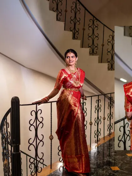 A graceful portrait of a South Indian bride in a stunning red silk saree, posing on a spiral staircase. Her traditional attire and elegant posture are simply timeless.