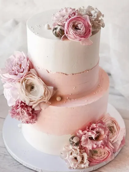A two-tiered cake with a soft pink ombre effect and adorned with beautiful ranunculus sugar flowers. Learn to create this romantic, textured look.