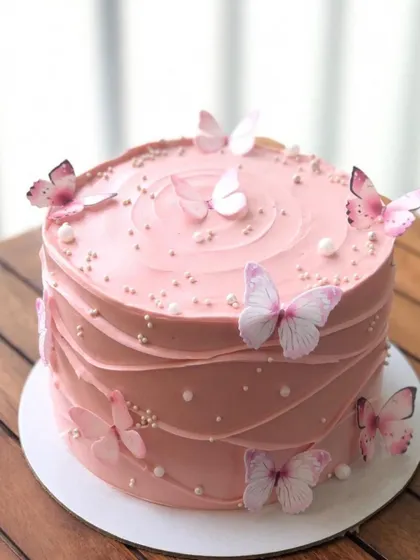 A simple pink cake with a textured wave design and delicate edible butterflies.