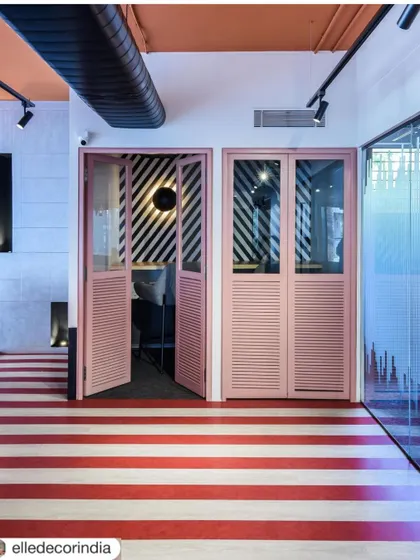 Playful design elements like these pink louvered doors and striped flooring define the private phone booths. These details add a pop of color and personality, making even the most functional spaces feel unique.