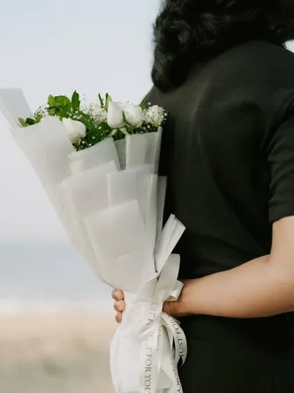 A sweet surprise moment during a proposal shoot, with the groom hiding a bouquet of white roses.