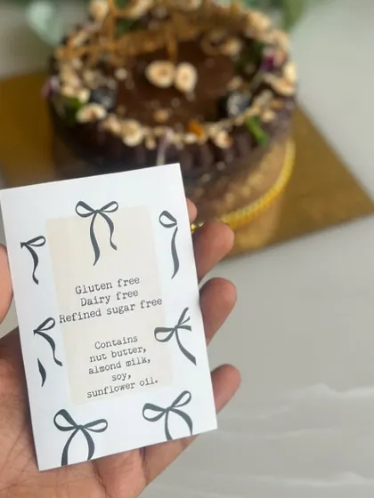 We believe in transparency. This card details the ingredients of one of our healthy cakes, showing that it's gluten free, dairy free, and refined sugar free, while also noting potential allergens like nut butter.