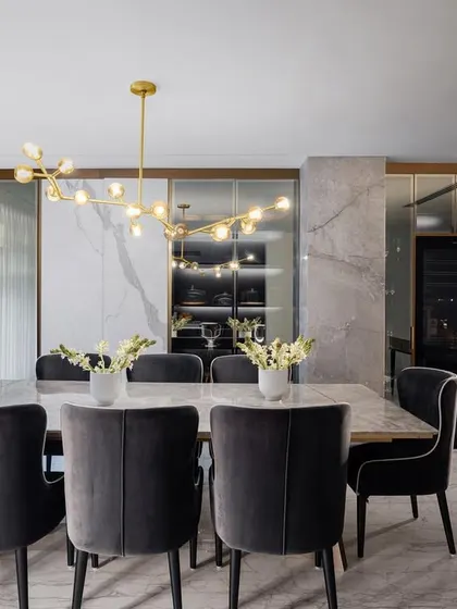 The dining room in the Amara residence, featuring plush velvet chairs and a modern brass chandelier. Mirrored panels behind the dining area create a sense of depth and reflect the natural light from the adjacent windows.