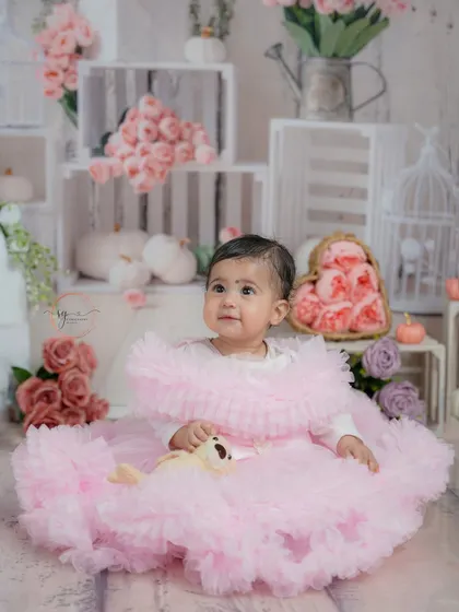 A full portrait in her beautiful pink dress, surrounded by a rustic setup of white crates and pink flowers.