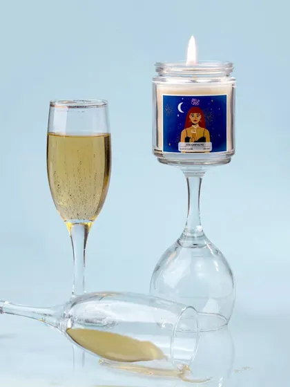 A creative and slightly playful shot, with the champagne candle balanced on an inverted wine glass. The spilled champagne adds a touch of drama and spontaneity to the scene.