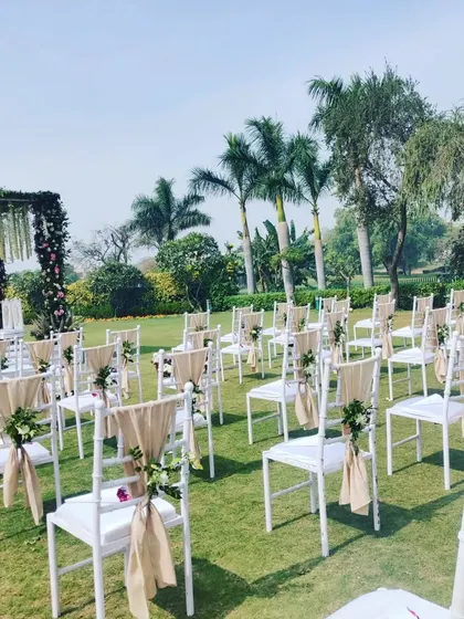 A clear view of the ceremony seating area on a lush green lawn. The chairs are neatly arranged with ample space, ensuring guests have a comfortable view of the proceedings.