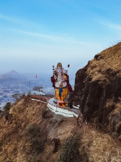 An aerial shot of a giant Ganesha statue on a mountainside, a perspective that shows its scale and the stunning landscape surrounding it.