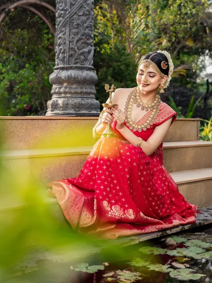 A serene shot of the bride in her red half-saree and temple jewellery, holding a traditional lamp. This look is perfect for festive occasions.