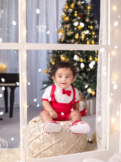 A little boy sits by the window, enjoying the view of the snow and the beautifully decorated Christmas tree.