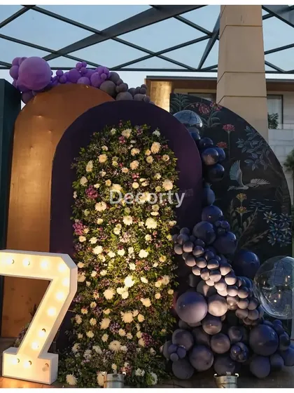 A modern take on a themed backdrop, combining a floral wall with a balloon cascade and a light-up number '7'.