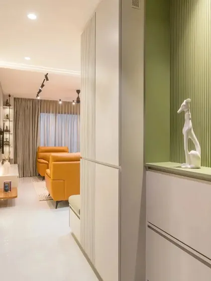 A minimal foyer with a green fluted shoe rack and storage unit, leading into a living room with a pop of color from an orange leather sofa.