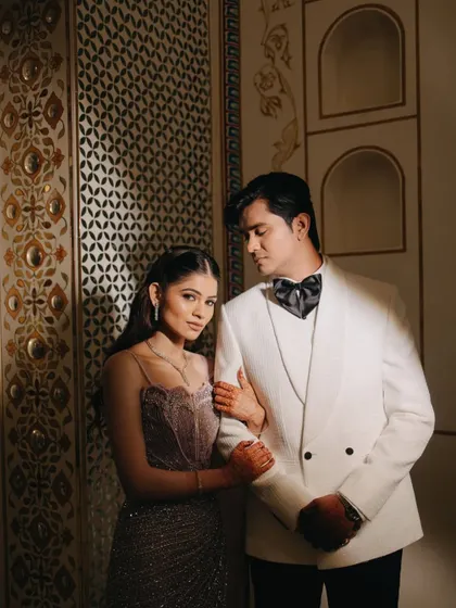 A classic, romantic portrait of the couple at their Sangeet, set against an ornate, palatial background.