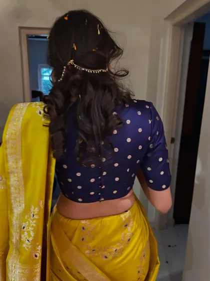 A back view of the heirloom look, showing the classic polka-dotted blouse paired with the vibrant yellow saree and a delicate hair accessory.