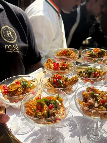 A server carries a tray of Kurkuri Bhindi chaat, served in individual glasses. This crispy okra snack is a modern and delicious take on a classic appetizer.