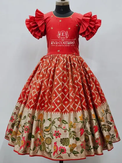 A beautiful red gown-style lehenga with dramatic ruffled sleeves. The skirt features a combination of ikat pattern and a wide, floral woven border.