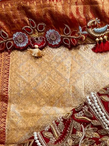 A detailed view of the custom tassels on this red bridal blouse, featuring a tiny embroidered bird. These personalized touches make each blouse one-of-a-kind.