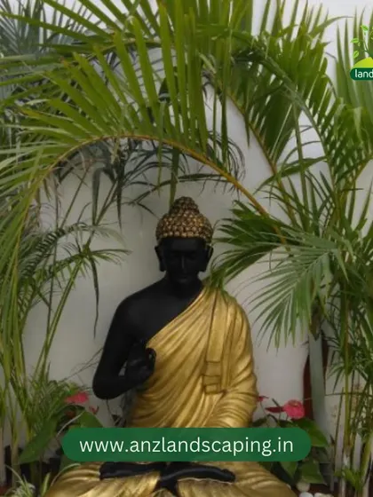 A tranquil garden corner featuring a Buddha statue nestled among palm fronds and white pebbles, creating a serene and meditative space.