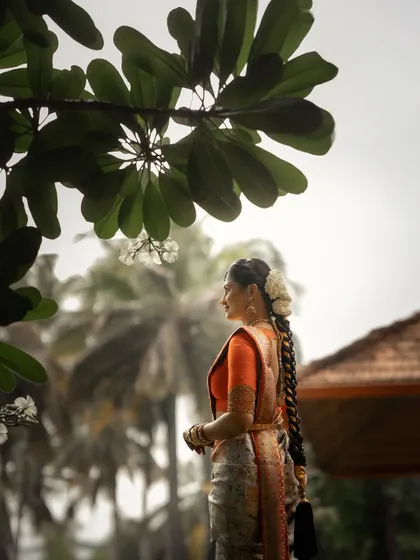 A side profile of a South Indian bride, framed by nature. The focus on her traditional braided hairstyle and the soft, natural light creates a timeless and elegant portrait.