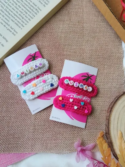 A closer look at our personalized pop-up hair clips for girls. This photo shows two different color schemes, a white clip for "Amirah" and a bright pink one for "Husna".