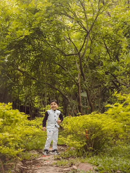 The vibrant green foliage makes this little boy in his smart outfit stand out. It's a perfect setting for a kids' outdoor photoshoot.