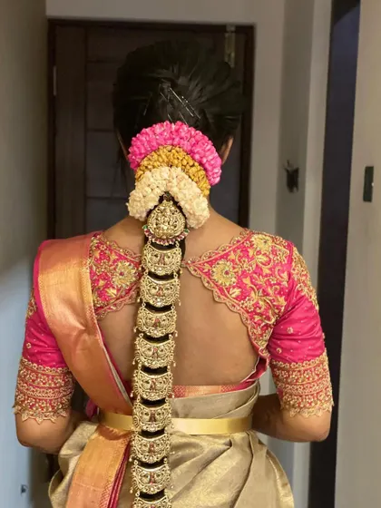 A full view of a traditional bridal braid, complete with a multi-colored flower arrangement and an elaborate gold jadai from top to bottom.
