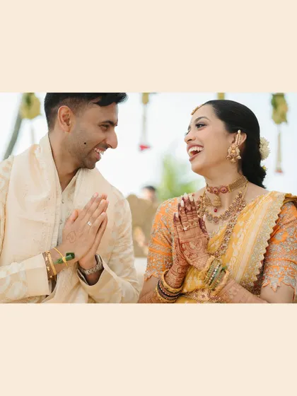 A joyful moment of greeting. The couple's shared laughter and 'namaste' gesture create a warm and welcoming photograph.