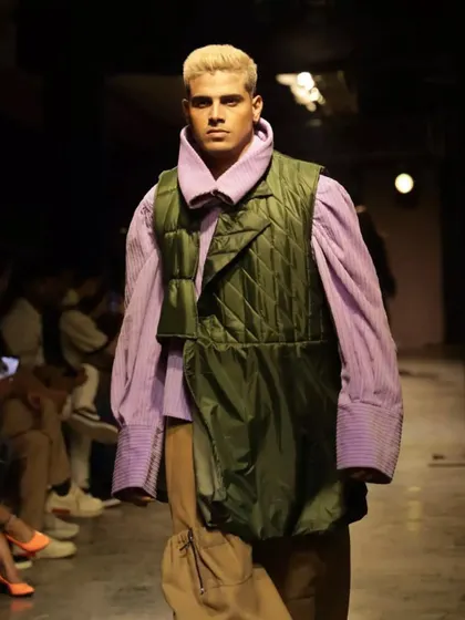 A clean, sharp makeup look for a male model at the FAD International show. The focus is on flawless skin and grooming to suit the modern, layered outfit.