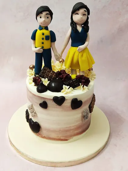We celebrate partnership with this sweet couple anniversary cake. A custom-made topper of the couple holding hands sits atop a cake decorated with chocolate hearts and bars, creating a personalized and romantic tribute to their love story.