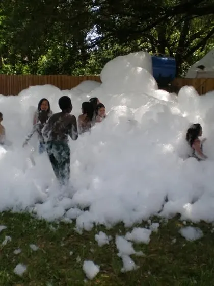 Kids having a blast in a mountain of foam at an outdoor party. This activity is pure fun and perfect for creating an energetic and playful atmosphere.