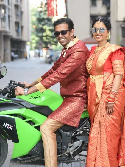 A stylish portrait of the newlywed couple with the groom on the bike and the bride standing beside him, both looking sharp in their sunglasses.