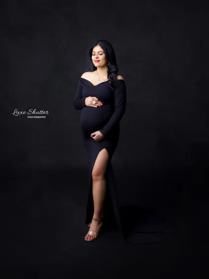 A quiet, contemplative pose that radiates grace. The simplicity of the black gown and dark background puts all the focus on the mother-to-be and her beautiful journey.
