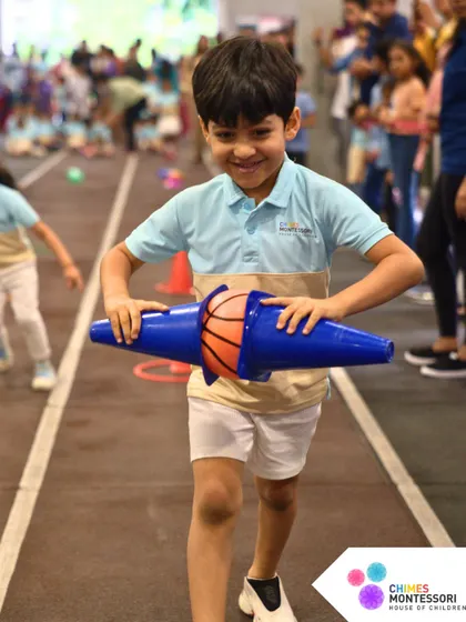 A child proudly carries his equipment during a Sports Day game, his smile showing his enjoyment and sense of accomplishment.