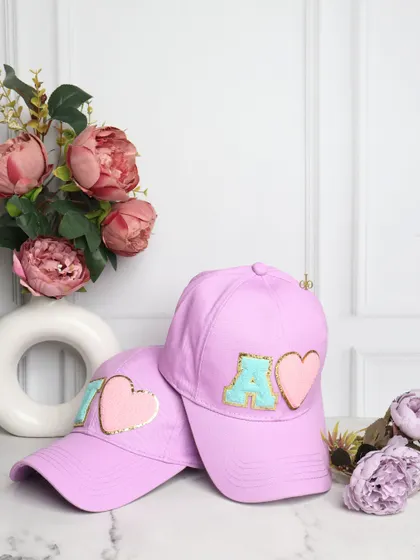 Your style, your initial. These trendy lilac baseball caps are customized with chenille initial and heart patches, making them a cute and personal accessory.