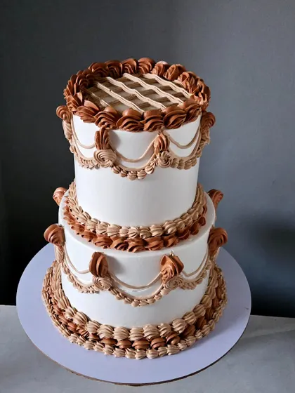 I have a deep appreciation for classic techniques. This two-tiered cake showcases my vintage piping skills, with intricate shell borders, swags, and lattice work, all piped by hand in beautiful boho shades of cream.