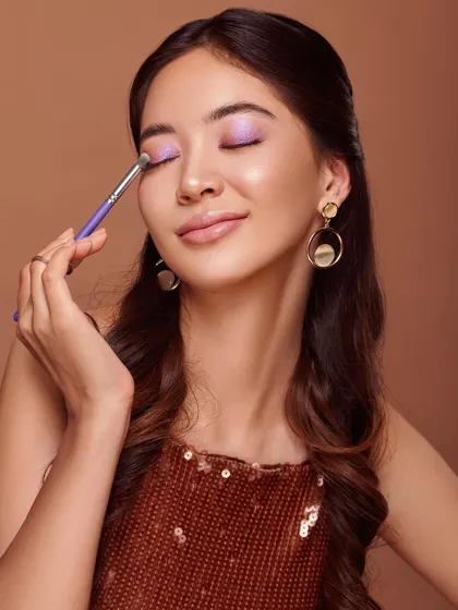 This image captures a moment of pure enjoyment in makeup application. The model has her eyes closed, smiling softly as she applies a shimmery lilac eyeshadow. It’s a beautiful shot that associates the product with a feeling of pleasure and self-expression.