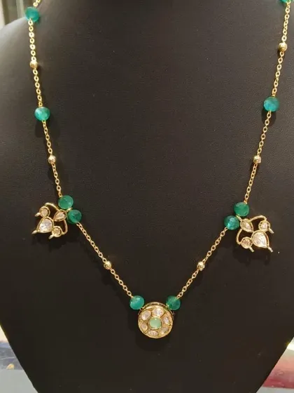 A simple gold chain necklace with Kundan charms and green beads. It's lightweight and stylish, making it suitable for both work and casual outings.