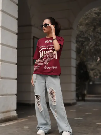 This lifestyle shot captures the full outfit, including the graphic tee, ripped baggy jeans, and sunglasses. The model's pose feels natural and gives a clear view of how the pieces work together.