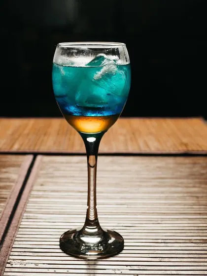 A layered cocktail with blue and yellow liquids in a tall glass. This beverage shot uses lighting to emphasize the vibrant colors and cool refreshment of the drink.