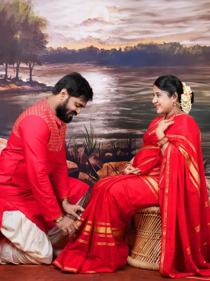 The dad-to-be kneels to adjust the mom-to-be's anklet, a gesture of care and affection that makes for a unique and heartfelt traditional portrait.