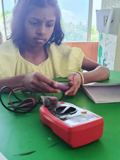 A focused student uses a multimeter to check her components. We empower kids to test and validate their own work, building independence and problem-solving skills.