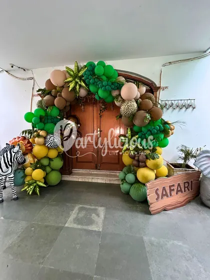An impressive balloon arch in jungle tones frames a doorway, with a friendly zebra and a safari sign welcoming guests to the adventure.